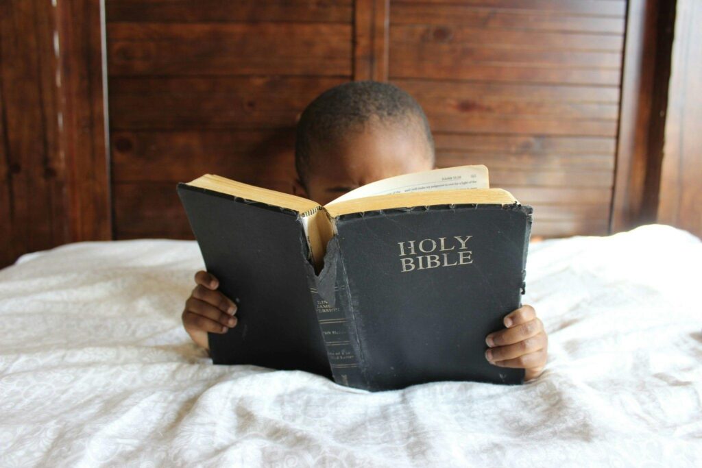 Young child reading a Holy Bible indoors, conveying a serene and religious atmosphere.